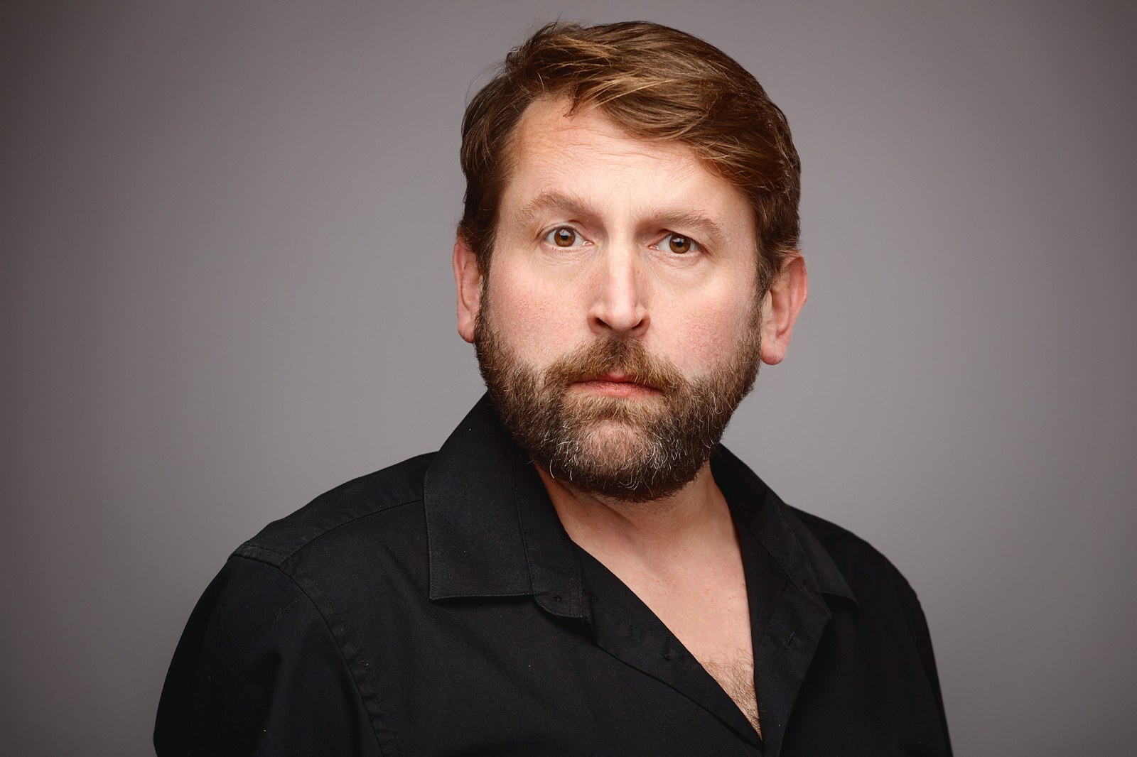 Lee Caley, studio headshot in a black shirt against a grey background